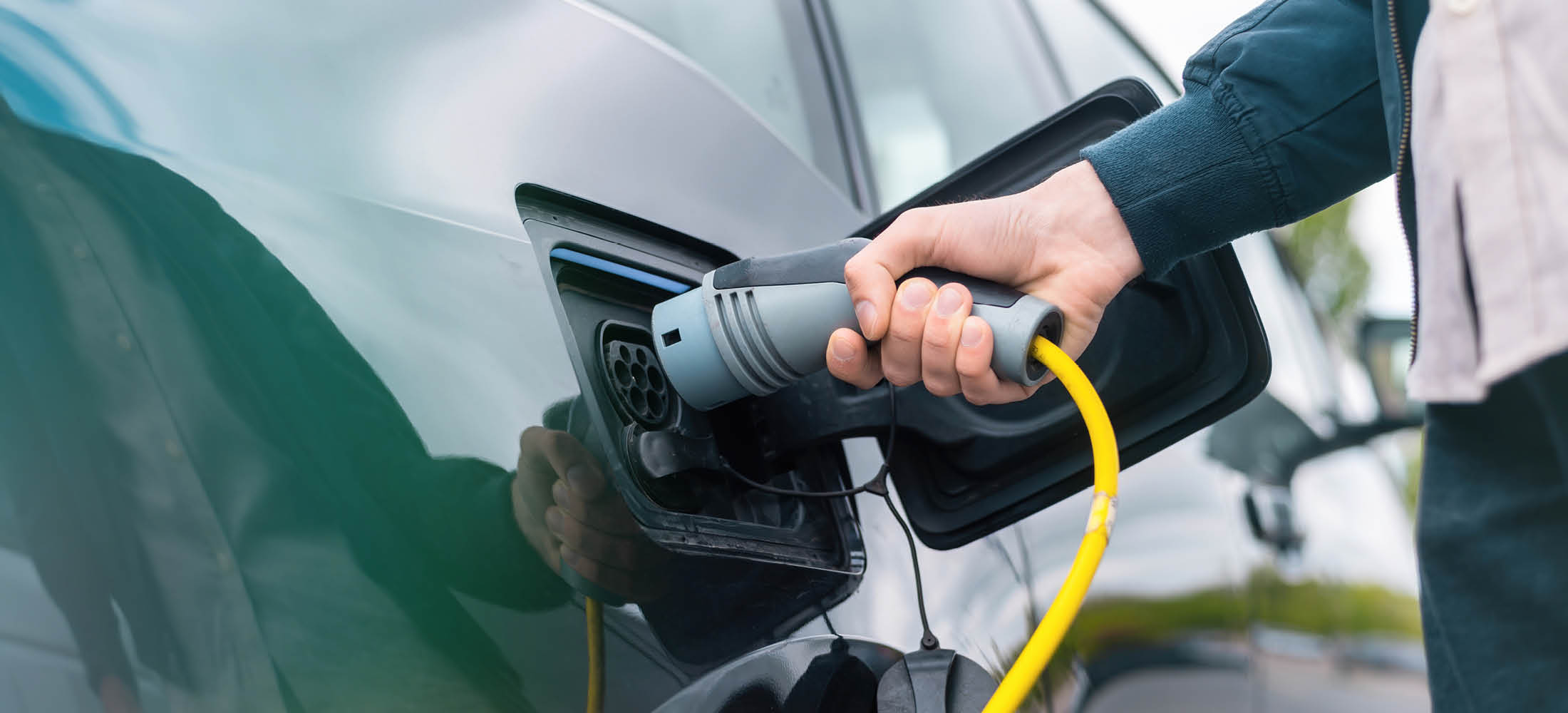 Eine Hand steckt ein Ladekabel mit gelbem Kabel in die Ladebuchse eines Elektroautos.